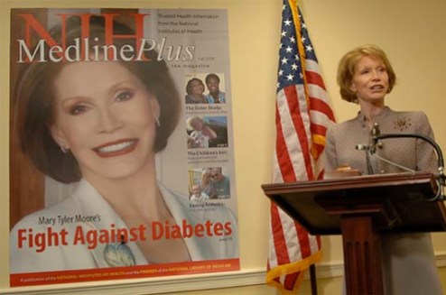Mary Tyler Moore stands at a podium. Visible to her right is a blow-up of the magazine cover featuring Moore.