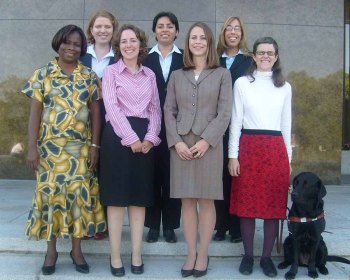 seven young women and a service dog pose for a formal group photo